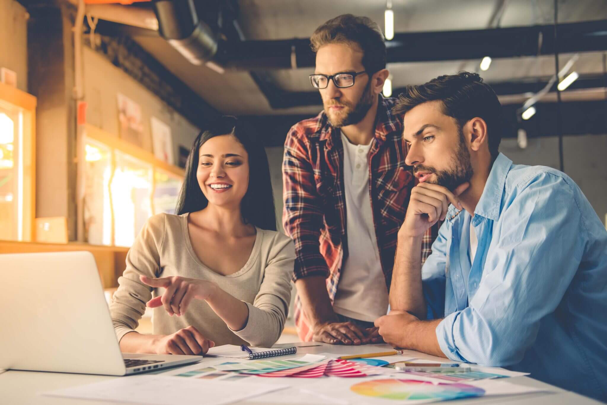 A woman and two men look at projects on a laptop