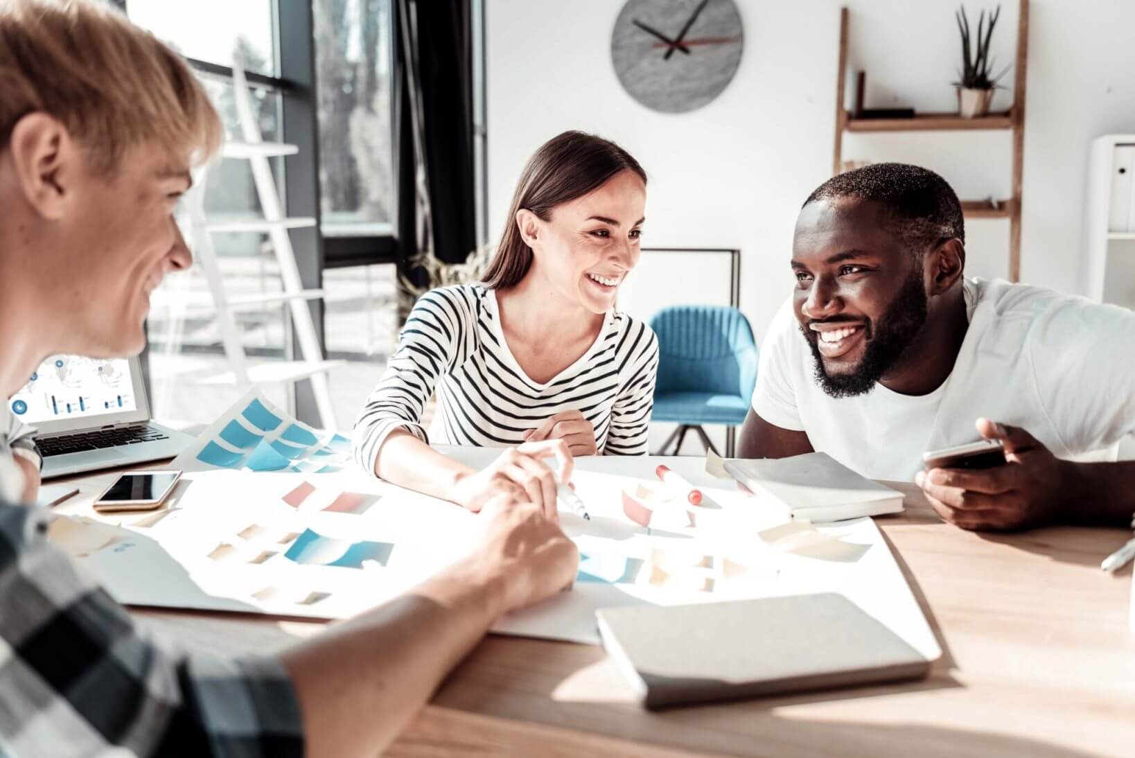 Three smiling people are discussing notes written on small colorful pieces of paper