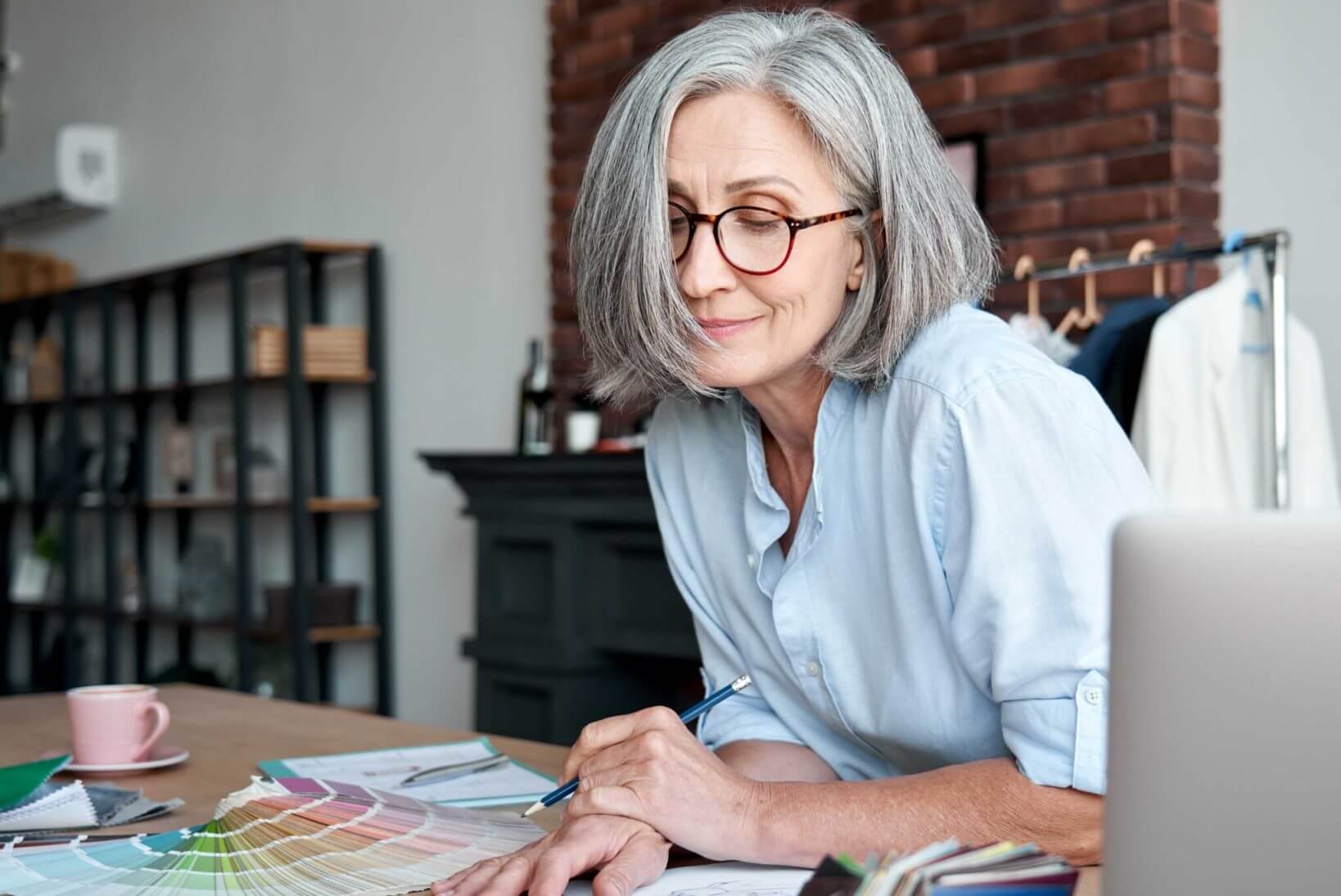 A woman with gray hair and glasses looks at paint samples