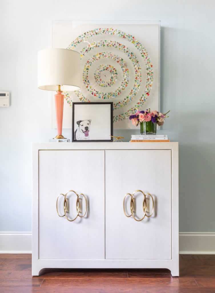 A white chest of drawers with an original painting hanging above it