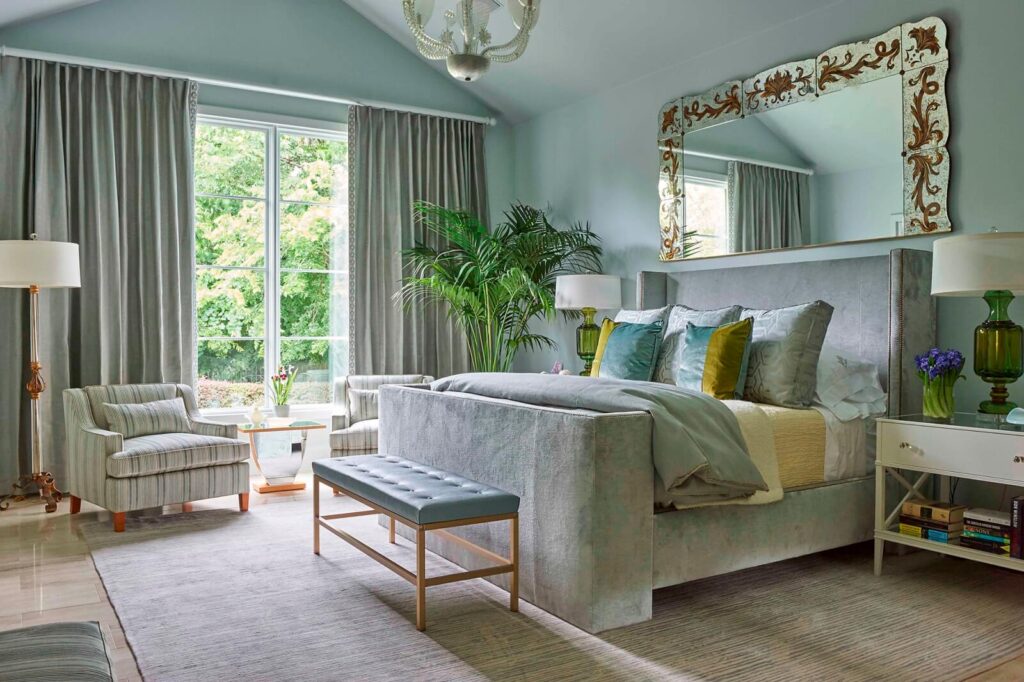 A bedroom with a large gray bed and a mirror hanging above the bed