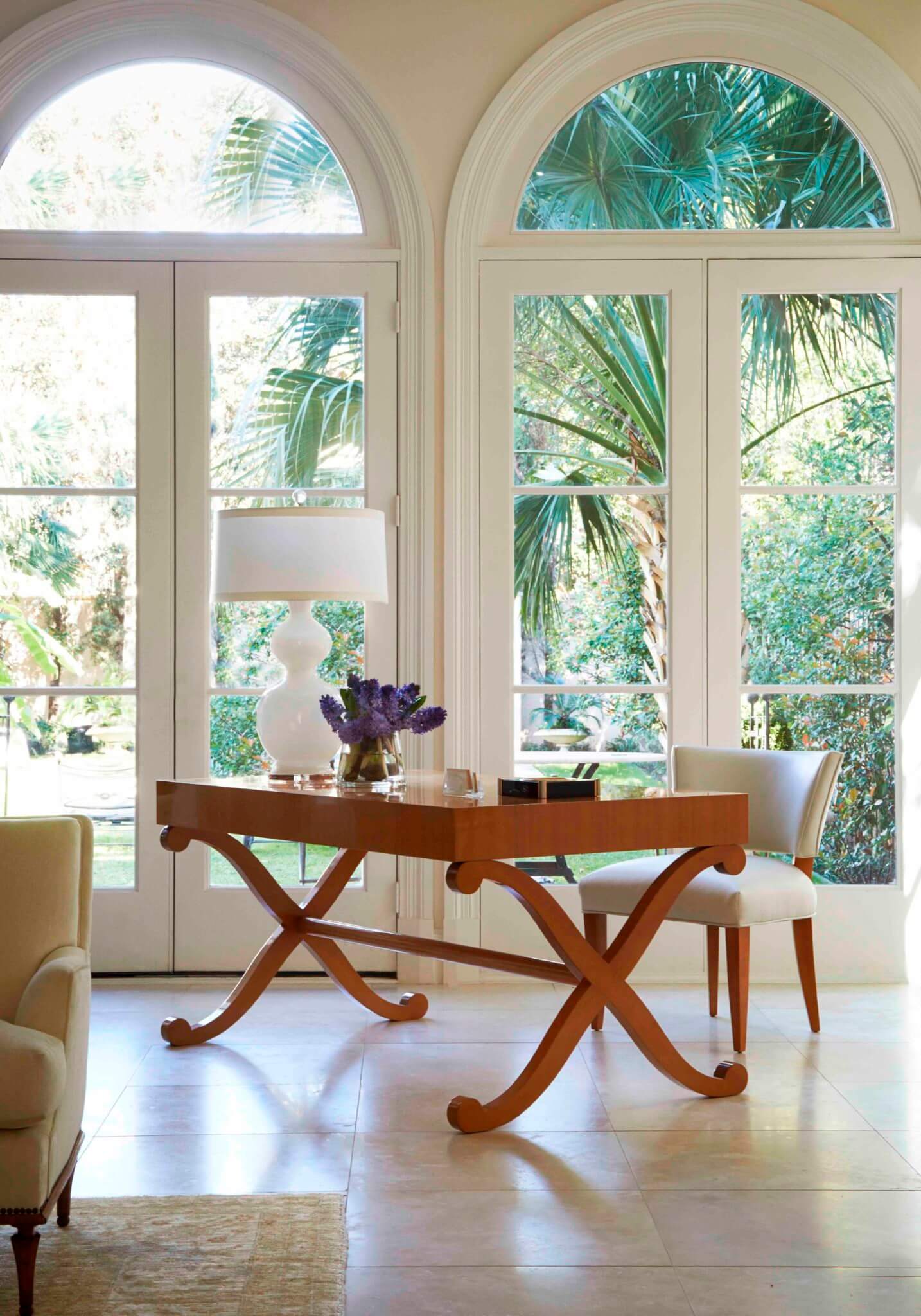 A wooden desk in a room with two huge windows overlooking a garden with palm trees